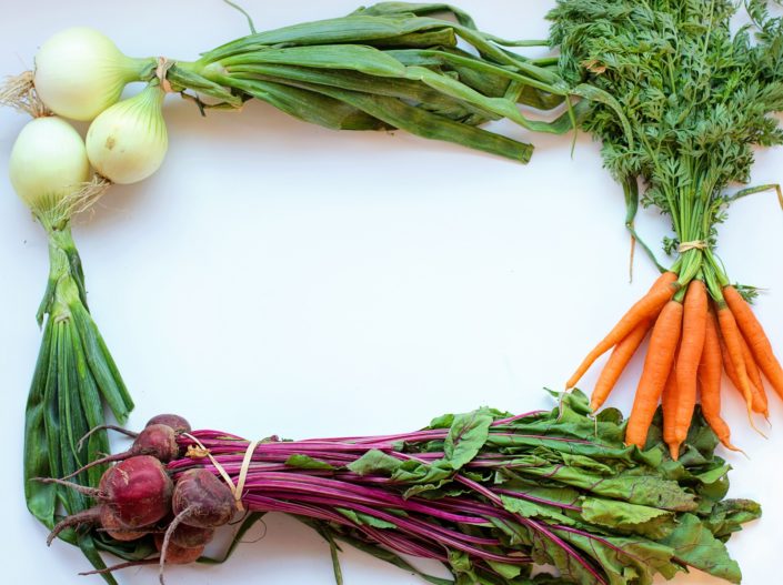 Fresh vegetables including onions, carrots, beets and green onions arranged in a frame shape on a white background