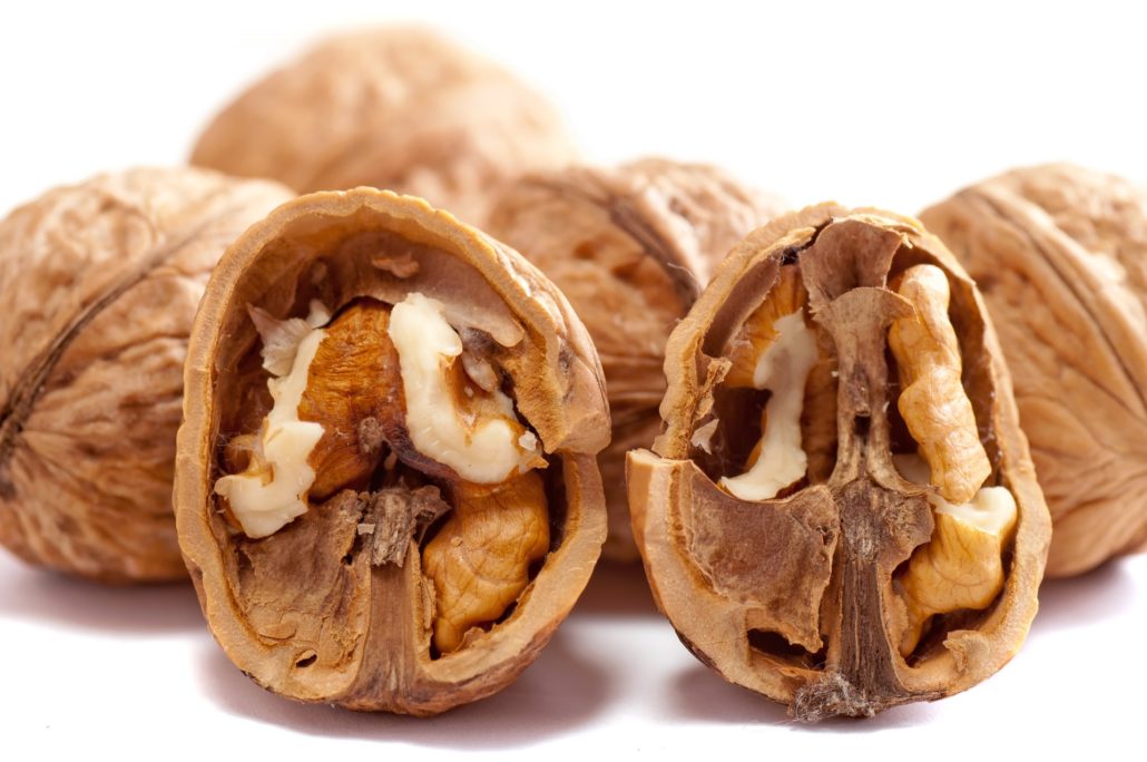 Cracked walnuts in shell showing pale nutmeat, surrounded by whole walnuts, neutral brown tones, simple still life