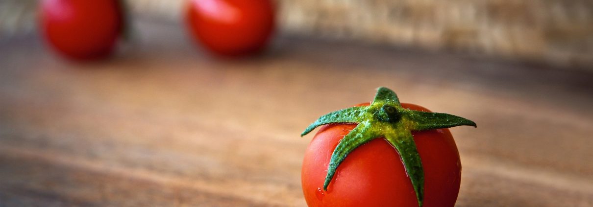 Close-up of a ripe red cherry tomato with green stem on a wooden surface, warm rustic mood